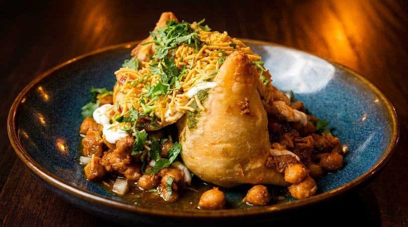 Samosa chaat with chickpeas, sauces, and crispy noodles, garnished with fresh cilantro.